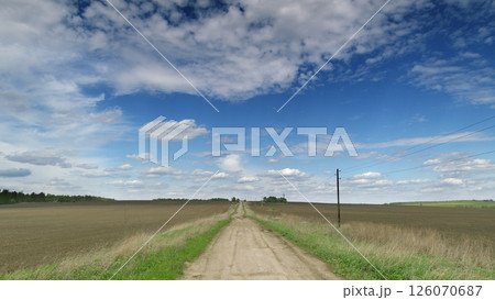 An Endless Dirt Road Meanders Through Lush Fields Beneath a Dramatic, Striking Sky Above 126070687