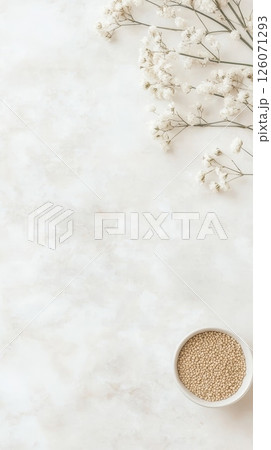 A bowl of small beige seeds sits on a marble surface next to delicate white flowers A bowl of small beige seeds sits on a marble surface next to delicate white flowers 126071293