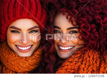 Two smiling women, bundled in warm winter scarves and hats, share a joyful moment outdoors 126071336