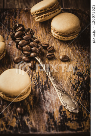 Delicious macarons arranged on a rustic wooden board with coffee beans and a vintage spoon, creating an inviting dessert scene for culinary enthusiasts and food lovers Delicious macarons arranged on a rustic wooden board with coffee beans and a vintage spoon, creating an inviting dessert scene for culinary enthusiasts and food lovers 126073625