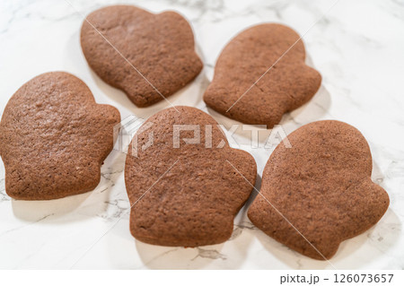 Angled close-up of four Pale Gingerbread Cookies shaped like mittens, highlighting their festive details and rich brown color. 126073657