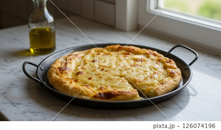 Homemade cheesy Greek pasta pie in round metal pan on marble windowsill with olive oil bottle 126074196