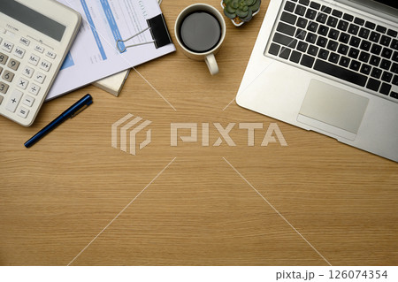 Modern office desk with laptop, calculator, coffee, and financial documents 126074354