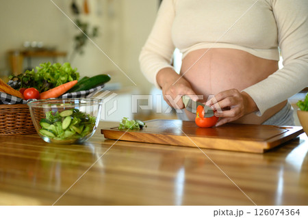 Pregnant woman preparing a fresh vegetable salad in the kitchen 126074364