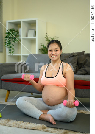 Pregnant woman working out indoors with small dumbbells 126074369
