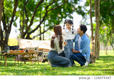 Happy family enjoying quality time together at a forest campsite with tents and picnic setup Happy family enjoying quality time together at a forest campsite with tents and picnic setup 126074387