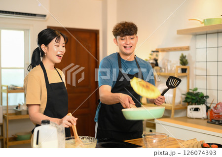 Man flipping pancake in a skillet while his partner watches and laughs Man flipping pancake in a skillet while his partner watches and laughs 126074393