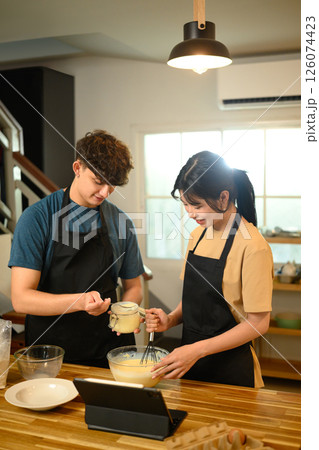 Cheerful young couple preparing breakfast pancakes in cozy home kitchen 126074423