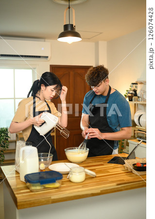 Young couple in aprons preparing pancake batter together in a cozy kitchen 126074428