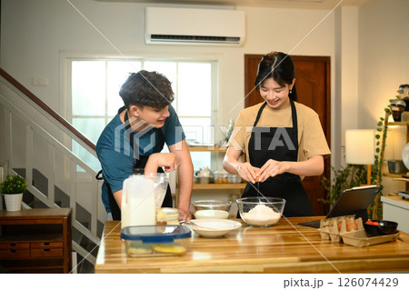 Happy couple cooking breakfast at home following digital recipe to make pancakes in a kitchen Happy couple cooking breakfast at home following digital recipe to make pancakes in a kitchen 126074429