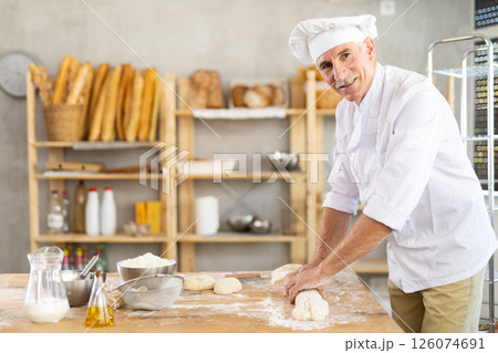 Elderly man baker rolls out dough Elderly man baker rolls out dough 126074691