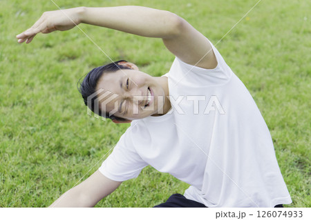 公園の芝生の上でストレッチをして苦しい顔をする若い男性 126074933
