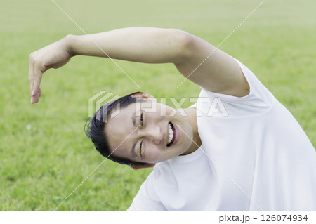 公園の芝生の上でストレッチをして苦しい顔をする若い男性 126074934