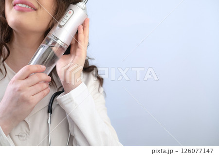 Female dentist shows a dental irrigator and explains how each part of the device helps care for oral hygiene. Female dentist shows a dental irrigator and explains how each part of the device helps care for oral hygiene. 126077147