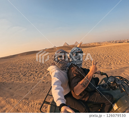 Tourists riding quad bike near giza pyramids at sunset, making peace sign 126079530