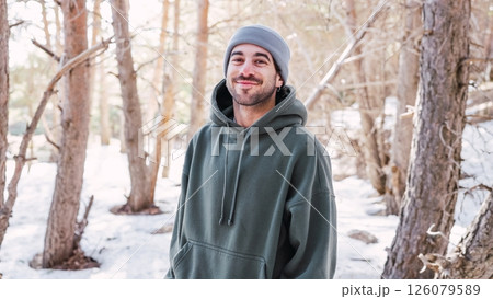 Young man smiling in snowy forest wearing hoodie and beanie 126079589