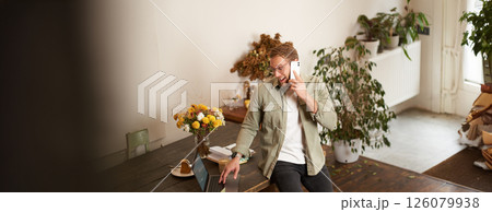 Portrait of happy young manager, man having negotiations, business conversation over the phone, talking on mobile, sitting in office on table with laptop 126079938