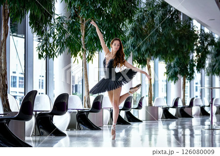 Graceful ballerina performing pose in modern interior with large windows 126080009