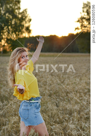 Woman meditating while sitting cross-legged in a golden wheat field during sunset hours for a sense of peace and tranquility 126080596