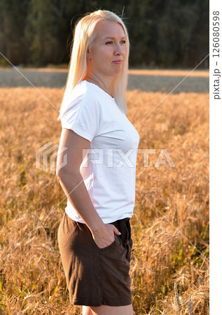 Woman stands in a golden field of wheat during sunset, showcasing natural beauty and serenity in a rural setting Woman stands in a golden field of wheat during sunset, showcasing natural beauty and serenity in a rural setting 126080598