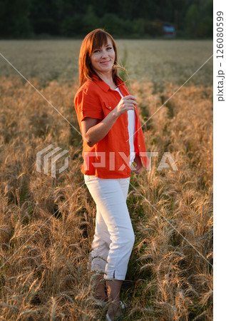 Woman with long hair in pink dress stands in golden wheat field during sunset, highlighting natural beauty and serene landscape 126080599