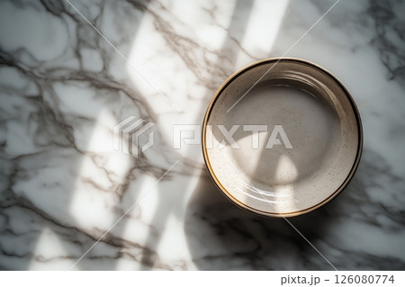 Shallow ceramic bowl on a marble surface with sunlight casting intricate shadows around it 126080774