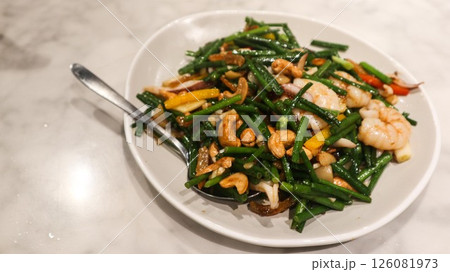Close up of Chinese dish stir fried dried shrimp, chives, prawns and cashew on a white plate with a spoon Close up of Chinese dish stir fried dried shrimp, chives, prawns and cashew on a white plate with a spoon 126081973