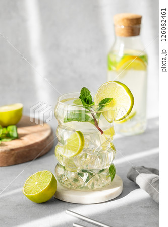 Mojito cocktail in a glass with lime, mint and ice on a textured background with natural light Mojito cocktail in a glass with lime, mint and ice on a textured background with natural light 126082461