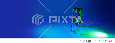 Dynamic image of man, professional cyclist in motion, riding bicycle against blue background with green neon light. Dynamic image of man, professional cyclist in motion, riding bicycle against blue background with green neon light. 126083058
