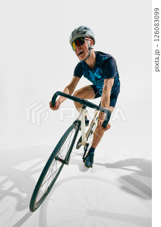 Full-length dynamic image of young man, professional cyclist in motion, training isolated on white background. Full-length dynamic image of young man, professional cyclist in motion, training isolated on white background. 126083099