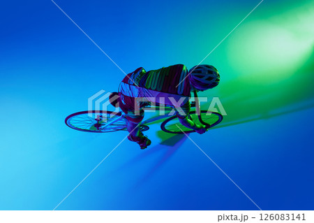 Top view of professional male cyclist in motion, training against blue studio background with green neon light. Top view of professional male cyclist in motion, training against blue studio background with green neon light. 126083141