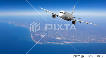 White passenger airplane flying over coastal area on sunny day 126083857