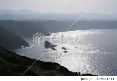Scenic coastal view of rugged cliffs and rocky shoreline at sunrise or sunset with shimmering reflections on the ocean surface 126084744