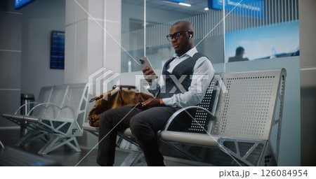 Departure Lounge of Airline Hub: Businessman with Bag Using Smartphone Departure Lounge of Airline Hub: Businessman with Bag Using Smartphone 126084954