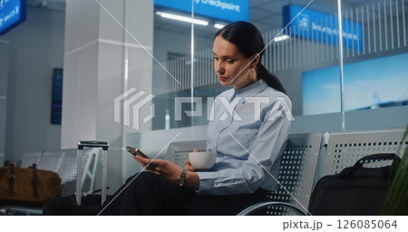 Businesswoman Using Smartphone and Drinking Coffee, Waiting for Flight in VIP Departure Lounge Businesswoman Using Smartphone and Drinking Coffee, Waiting for Flight in VIP Departure Lounge 126085064