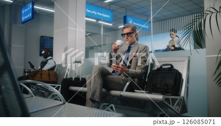 Airport Terminal: Successful Man Sitting in Departure Lounge, Using Cellphone and Drinking Coffee 126085071