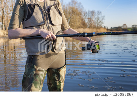 Fisherwoman wearing fishing waders holding fishing rod in river Fisherwoman wearing fishing waders holding fishing rod in river 126085867
