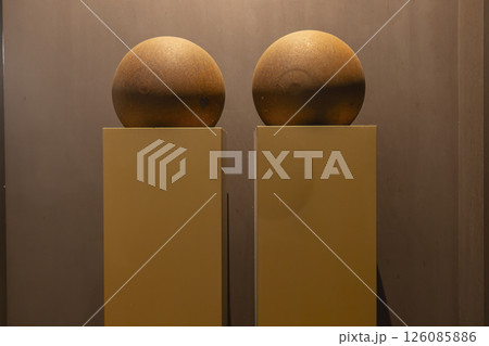 Modern art installation featuring two rusty spheres on yellow pedestals against a brown wall Modern art installation featuring two rusty spheres on yellow pedestals against a brown wall 126085886