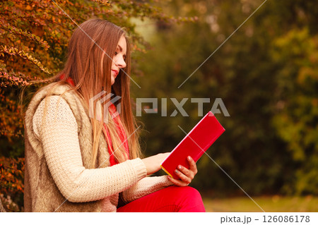 Woman relaxing in autumnal park reading book 126086178