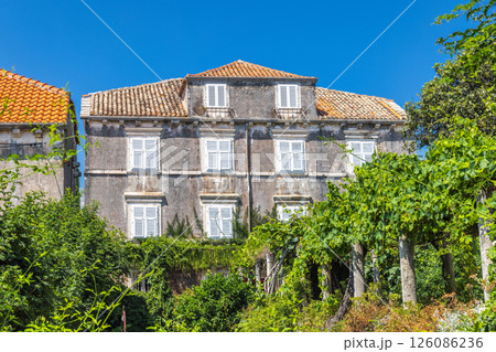 Orebic town at coast of the Peljesac peninsula in Croatia, Europe. Historic European villa with shuttered windows and tiled roof, surrounded by lush vegetation and a clear blue sky. Orebic town at coast of the Peljesac peninsula in Croatia, Europe. Historic European villa with shuttered windows and tiled roof, surrounded by lush vegetation and a clear blue sky. 126086236