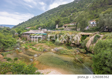 Bregava river in Stolac town, Bosnia and Herzegovina, Europe. Picturesque European river scene with lush greenery, traditional buildings, and a tranquil cascade. A serene landscape. Bregava river in Stolac town, Bosnia and Herzegovina, Europe. Picturesque European river scene with lush greenery, traditional buildings, and a tranquil cascade. A serene landscape. 126086362