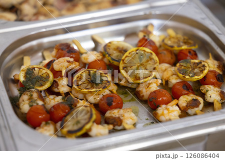 Grilled shrimp skewers with lemon and cherry tomatoes resting in a chafing dish Grilled shrimp skewers with lemon and cherry tomatoes resting in a chafing dish 126086404