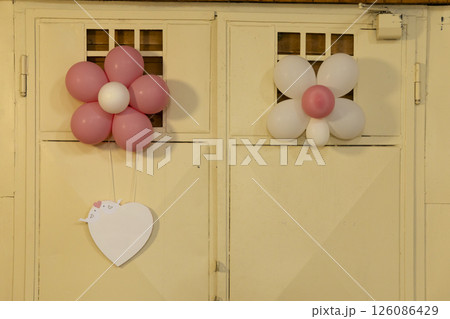 Pink and white flower shaped balloons hanging on a door with a heart shaped card 126086429