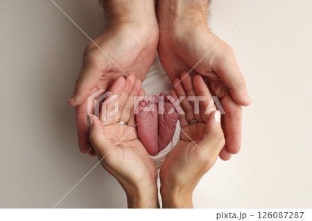 A father and mother hold the feet of a newborn child in a white blanket on a white background.. The feet of a newborn in the hands of parents. Photo of foot, heels and toes.The palms of the parents. A father and mother hold the feet of a newborn child in a white blanket on a white background.. The feet of a newborn in the hands of parents. Photo of foot, heels and toes.The palms of the parents. 126087287