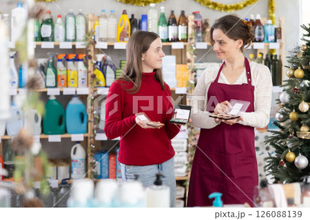 Saleswoman helping teenage girl select makeup in Christmas decorated store Saleswoman helping teenage girl select makeup in Christmas decorated store 126088139