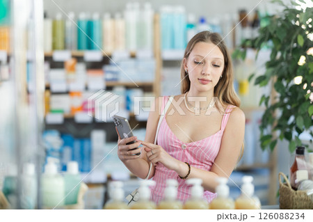 Woman in summer dress with phone in hands in pharmacy Woman in summer dress with phone in hands in pharmacy 126088234