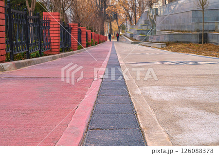 Close-up street strip of pedestrian sidewalk from lower angle with passage of cyclists. Horizontal shot with random two unrecognizable blurred silhouettes of people in the background 126088378