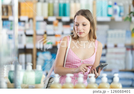 Woman in summer dress with phone in hands in pharmacy Woman in summer dress with phone in hands in pharmacy 126088401