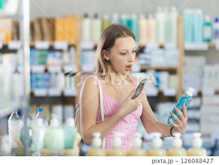 Blonde woman scanning on mobile bottle with rinse aid Blonde woman scanning on mobile bottle with rinse aid 126088427