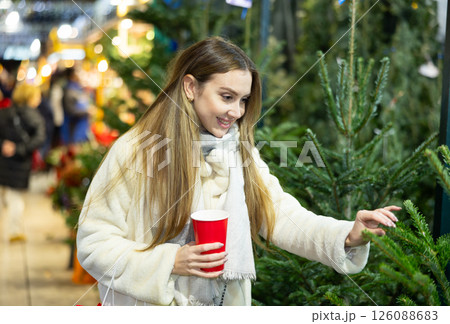 Young woman at spruce bazaar examines branches of live fir tree. Young woman at spruce bazaar examines branches of live fir tree. 126088683